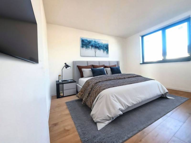 Bedroom in a family house with a bed, painting, TV, and floor with wooden decor.