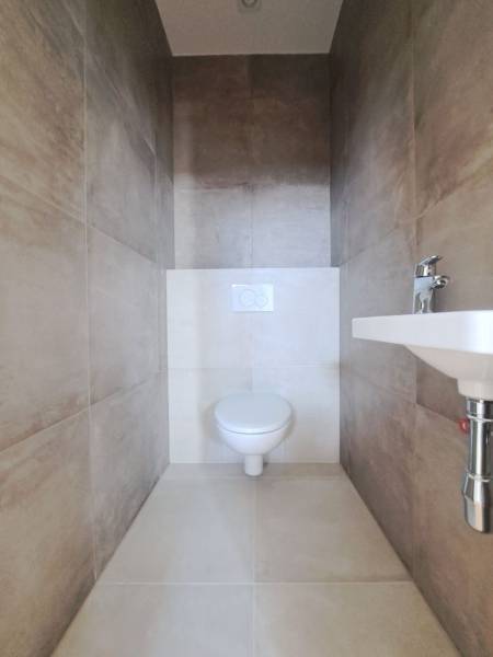 A toilet in a family house with beige ceramic tiles and a sink.