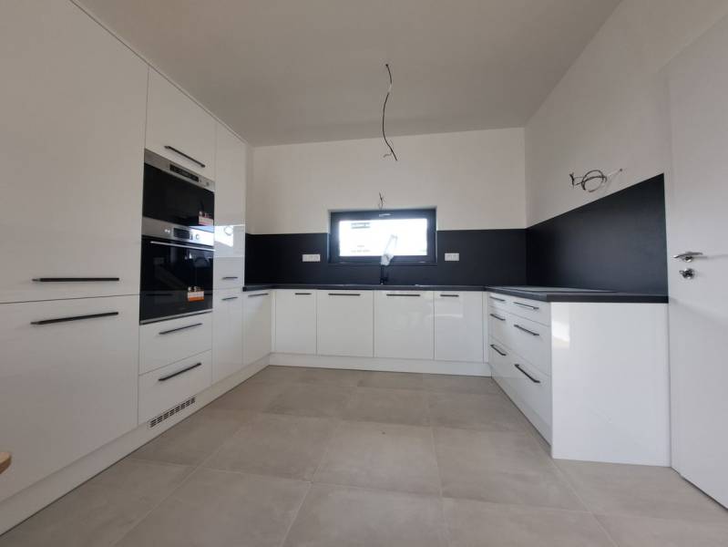 White kitchen unit and black tiles in a family house with a window and appliances.