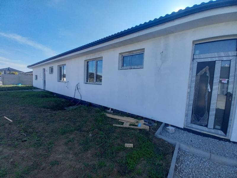 A family house in Galanta with a white facade, large windows, and an unfinished surrounding area.