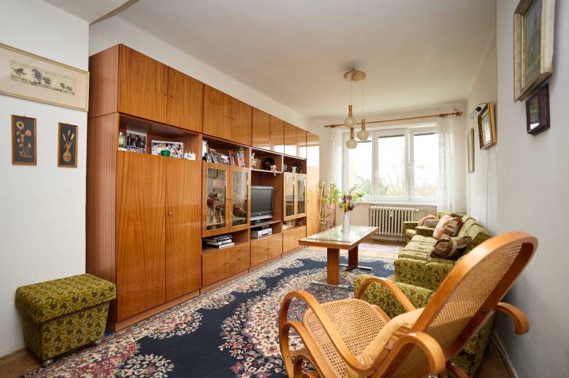 Living room with a carpet, wooden furniture, and a large window in a three-room apartment.
