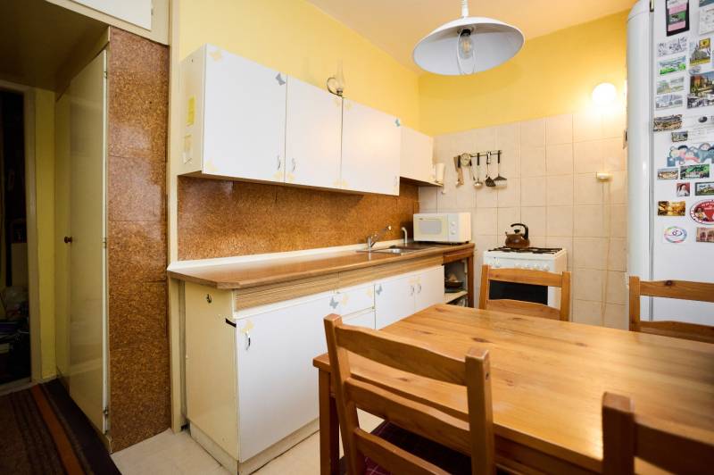 A kitchen with a wooden table in a three-room apartment. Cabinets, stove, refrigerator with magnets.
