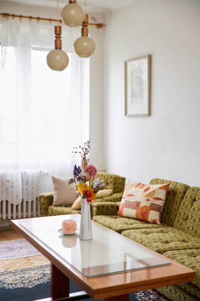 A bright living room in a three-room apartment with a sofa, table, and decorative flowers in a vase.