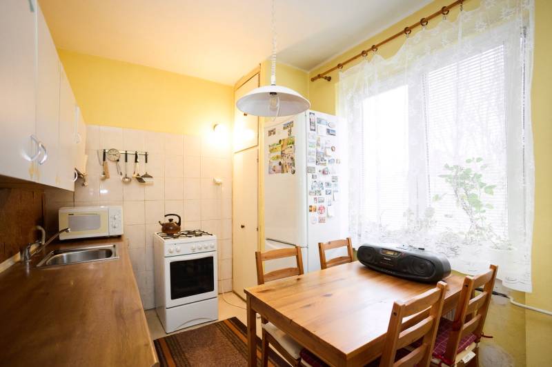 A kitchen in a 3-room apartment with a wooden table, a stove, and white cabinets.