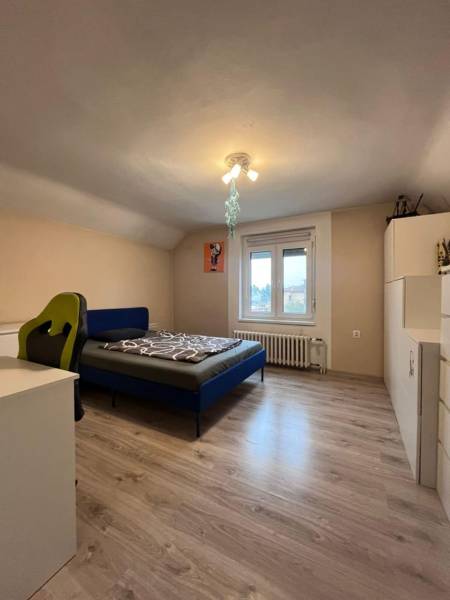 A bedroom in a family house with a wood-decor floor, a bed, and a desk.