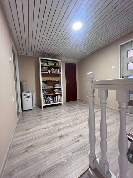 A hallway with a wood-patterned floor, a bookshelf, and light wooden railing in a family house.