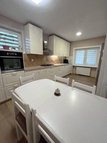 A kitchen in a family house with white furniture and a wooden decor floor.