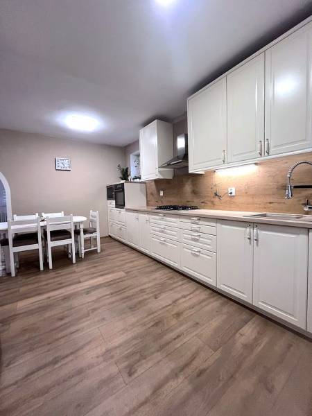 White kitchen with wood-patterned flooring in a family house. Dining table, wooden cabinets.