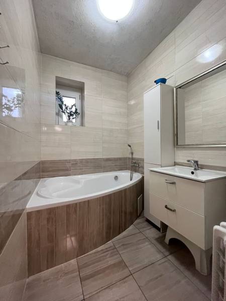 A bathroom with a bathtub in a family house, tiled walls, a window with a flower.