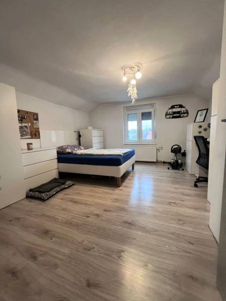 A bedroom in a family house with a bed, white furniture, and a floor with a wooden decor.