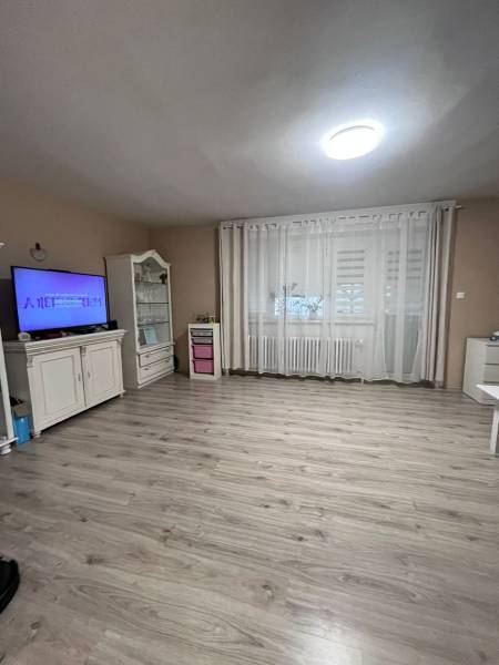 A room in a family house with a wooden decor floor, a television, and curtains.