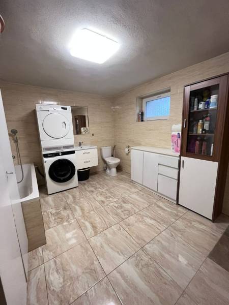 A bathroom in a family house with a washing machine, dryer, bathtub, and storage cabinets.
