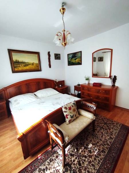 A bedroom in a family house with wooden furniture, a floor with a wooden decor, and paintings on the wall.