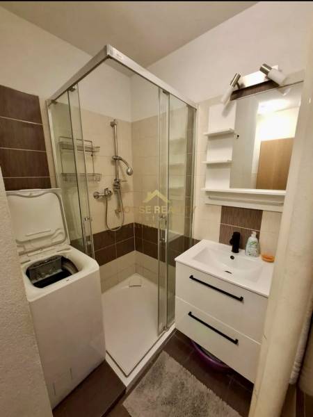Bathroom in a 4-room apartment with a washing machine, shower, and sink with storage space.