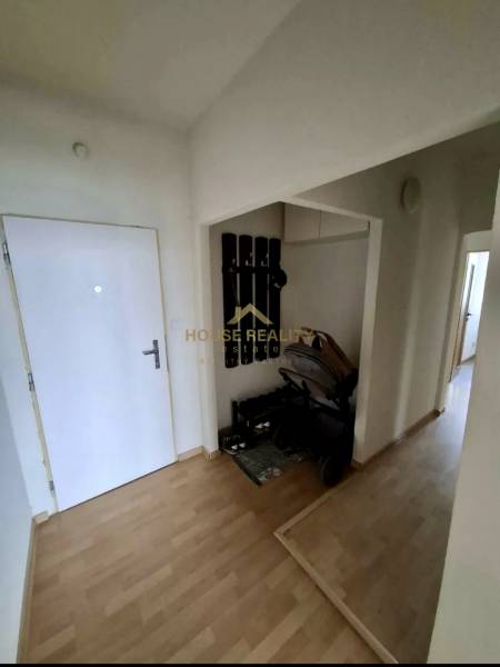 A hallway in a 4-room apartment with a coat rack, a stroller, and a wooden-patterned floor.