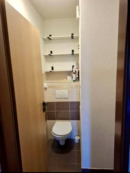 A toilet with wall shelves in a 4-room apartment, floor with wooden decor.