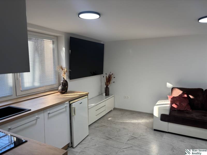 Living room in a family house with a white kitchen unit and a dark brown sofa.