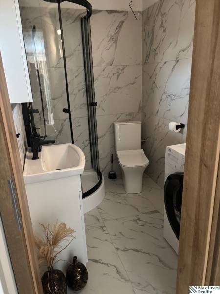 A bathroom in a family house with marble tiling, a shower cabin, and a washing machine.