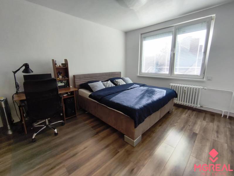 A room in a one-room apartment with a bed, a table, and a floor with a wooden decor.