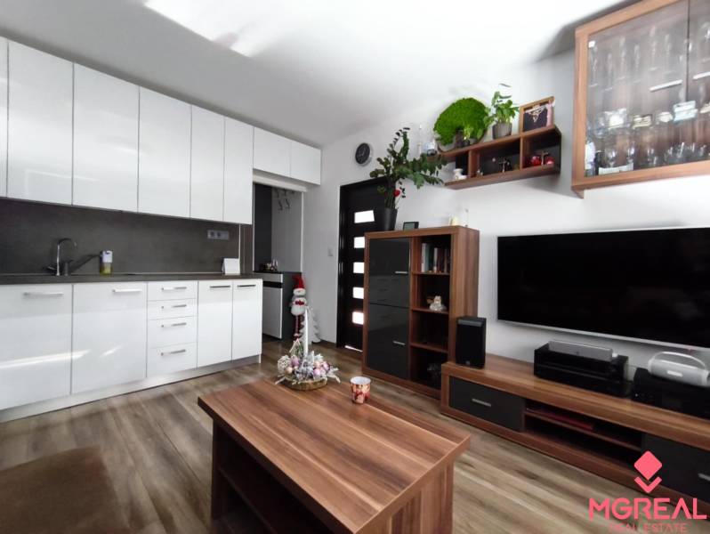 A kitchenette with white cabinets, a television, furniture, and a wooden decor floor in a studio apartment.