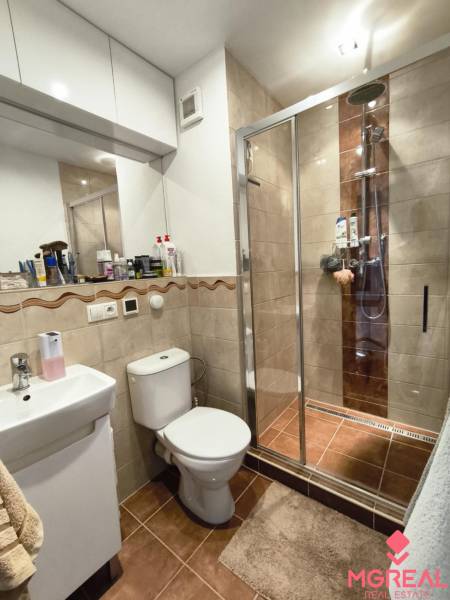 Bathroom of a one-room apartment, shower corner, sink, toilet, and cabinets.