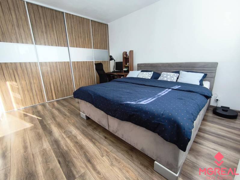 A bedroom in a studio apartment with a wood-patterned floor and built-in wardrobes.