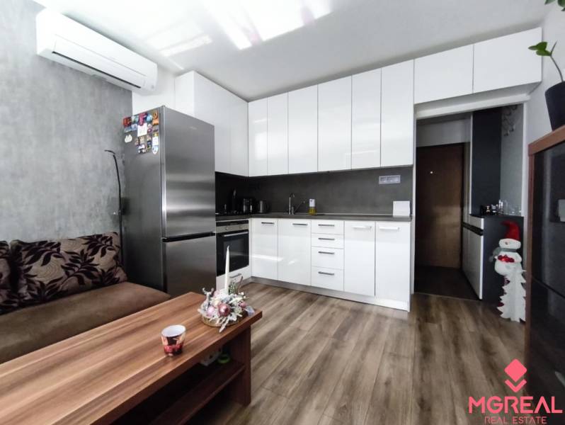 A kitchen in a studio apartment with a wood-patterned floor, white cabinets, and a sofa.