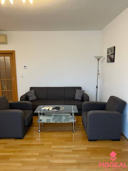 Gray sofa in a 3-room apartment with wood-patterned flooring and a glass table.