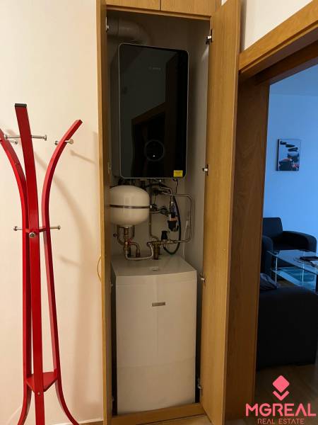 A water heater in the closet next to the red hanger in a 3-room apartment.
