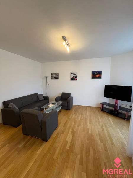 Living room in a three-room apartment with a wooden decor floor, a sofa, and a television.