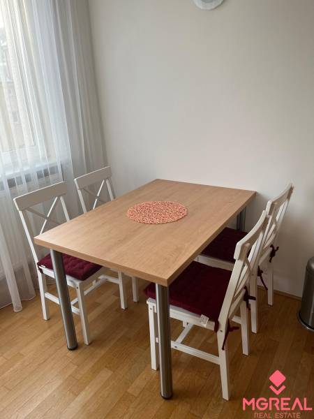 A dining table with four chairs and a wooden decor floor in a three-room apartment.