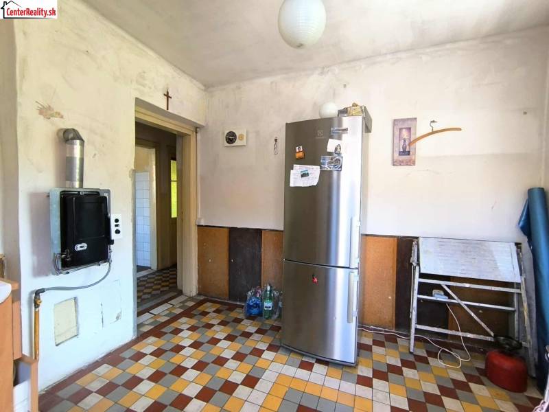 A kitchen in a family house with an older design, a refrigerator, and a tiled floor.