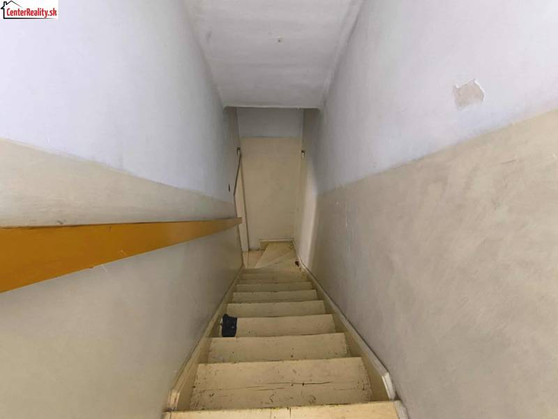 A narrow staircase in a family house with white walls and wooden railing.