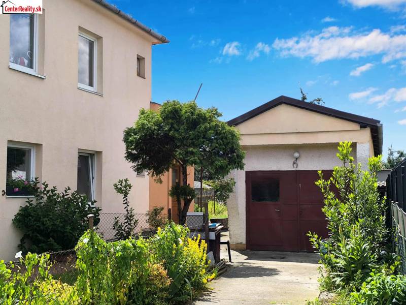 A family house in Partizánske with a garage surrounded by a garden full of green plants.