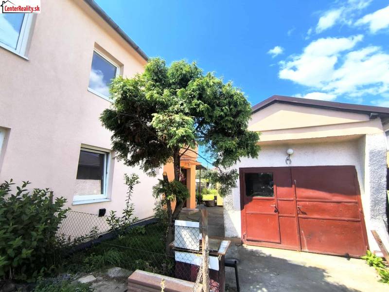 A family house in Partizánske with a garage, a green tree, and a well-fenced garden.