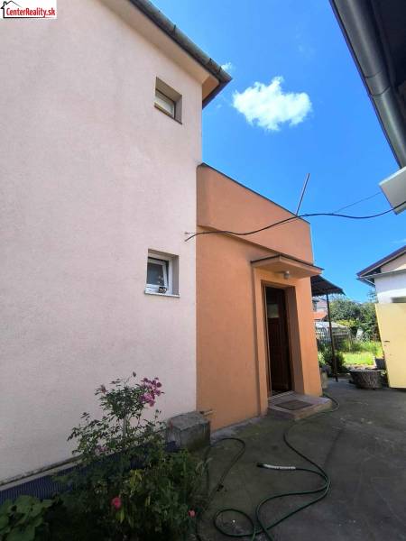 A family house in Partizánske with a yard, flowers, and a hose on a concrete walkway.