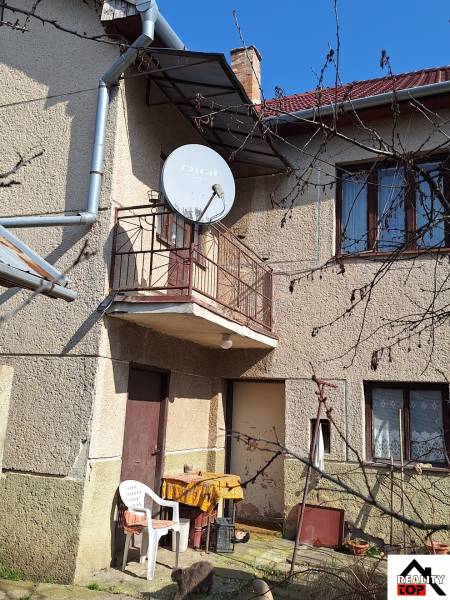 A family house in Tachtá with a balcony, satellite dish, and garden chairs under the blue sky.