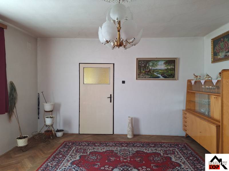 Living room in a family house with a carpet, chandelier, painting, and display cabinet.