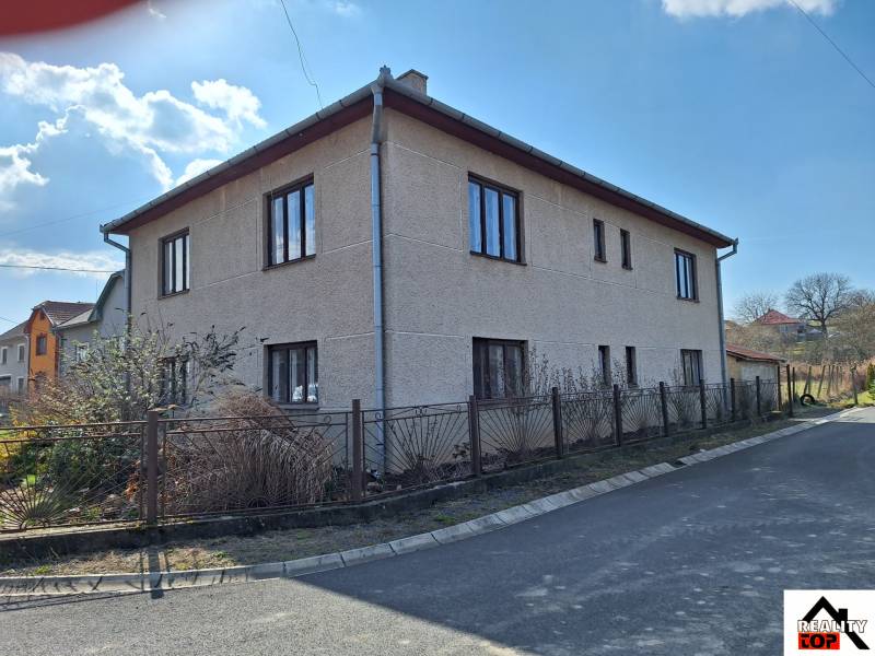 A family house in Tachtoch with plaster, next to the road and a metal fence.