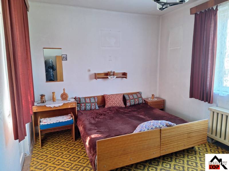 Bedroom in a family house with textile curtains, patterned carpet, and a bed.