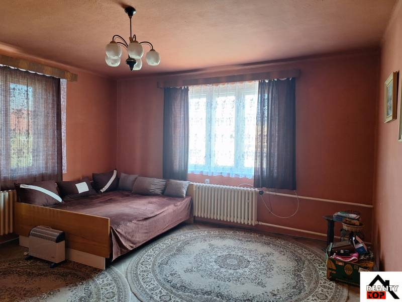 A room in a family house with a bed, carpet, curtains, and a nightstand.