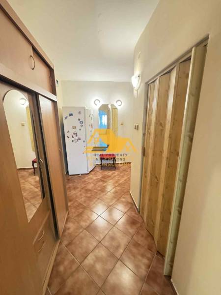 A hallway in a 3-room apartment with ceramic tiles, a built-in wardrobe, and a refrigerator in the background.