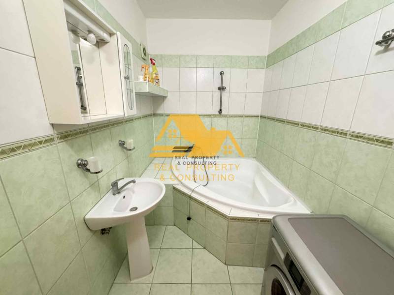 A bathroom in a 3-room apartment with a corner bathtub, sink, and washing machine.