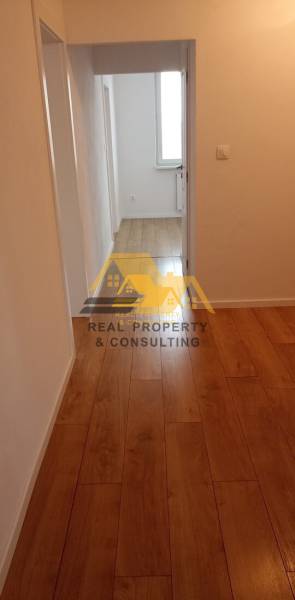 A hallway with a wood-patterned floor in a 2-room apartment, neutral walls.