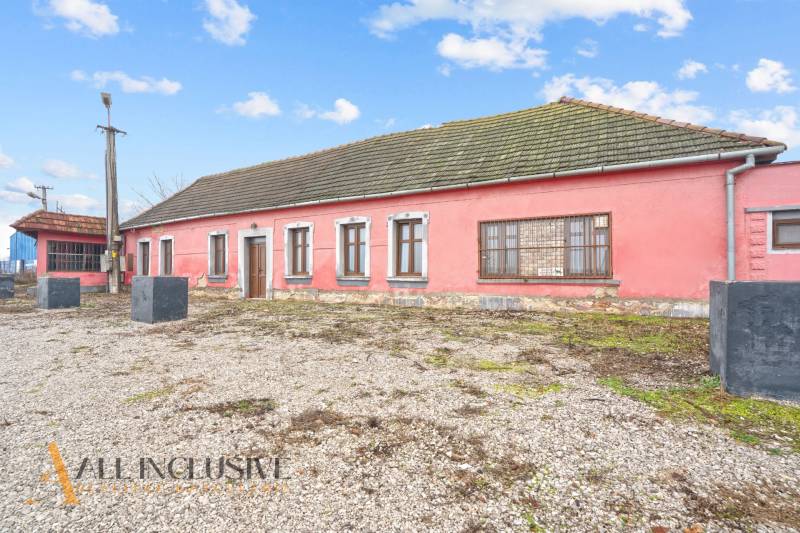 A family house in Šintava with a stone base, pink facade, and wooden windows.