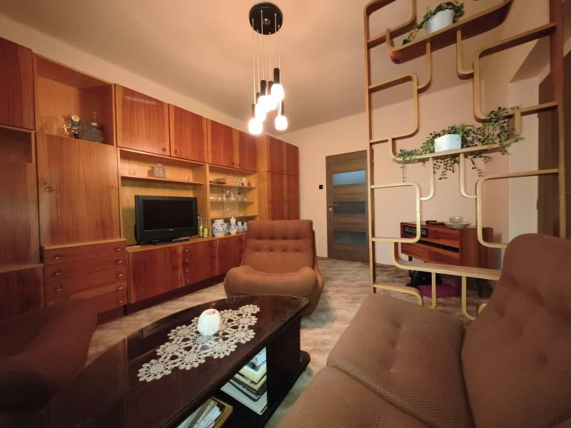 Living room in a 3-room apartment with wooden furniture and decorative shelves.