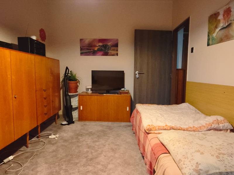 A room in a 3-room apartment with a carpeted floor, a bed, and wooden furniture.