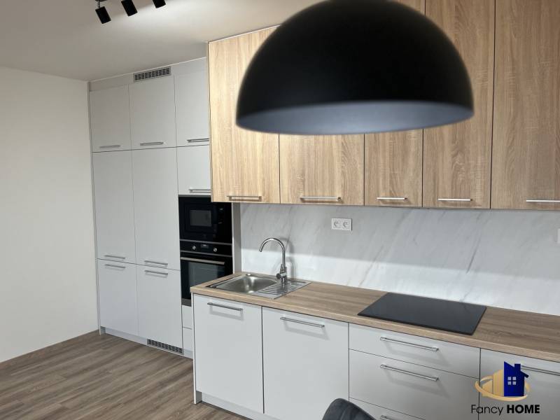 A kitchen in a two-room apartment with a wooden decor floor and light furniture.