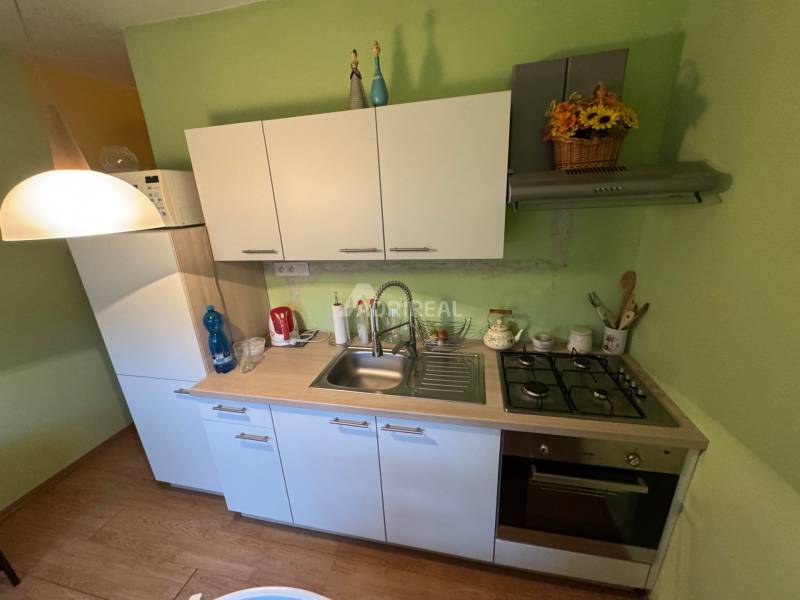 A kitchen in a studio apartment with white cabinets and a wood-patterned floor.