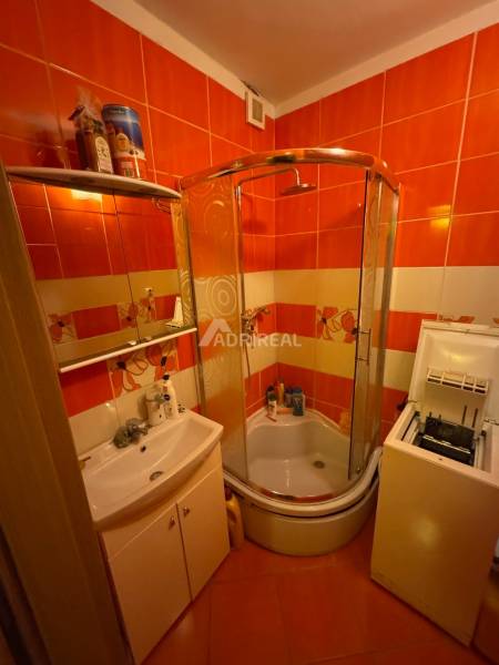 A bathroom in a studio apartment with orange tiles, a shower, and a sink.